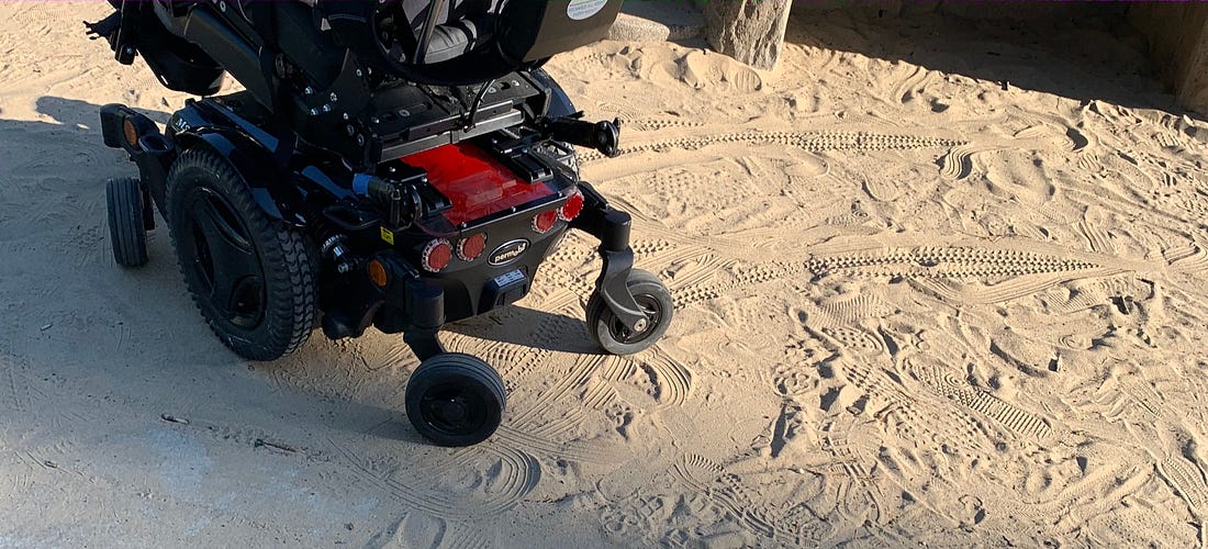 A power chair user makes tracks in sand. 