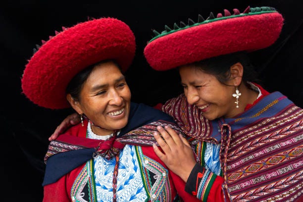 portrait of two local women who are close friends, in colourful, predominantly red, traditional local dress and hats, chinchero, sacred valley, peru (model releases) - indigenous culture stock pictures, royalty-free photos & images