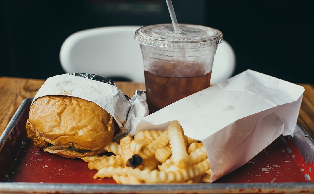 image of a burger, fries and fizzy drink on a tary for article by Larry G. Maguire on fitness