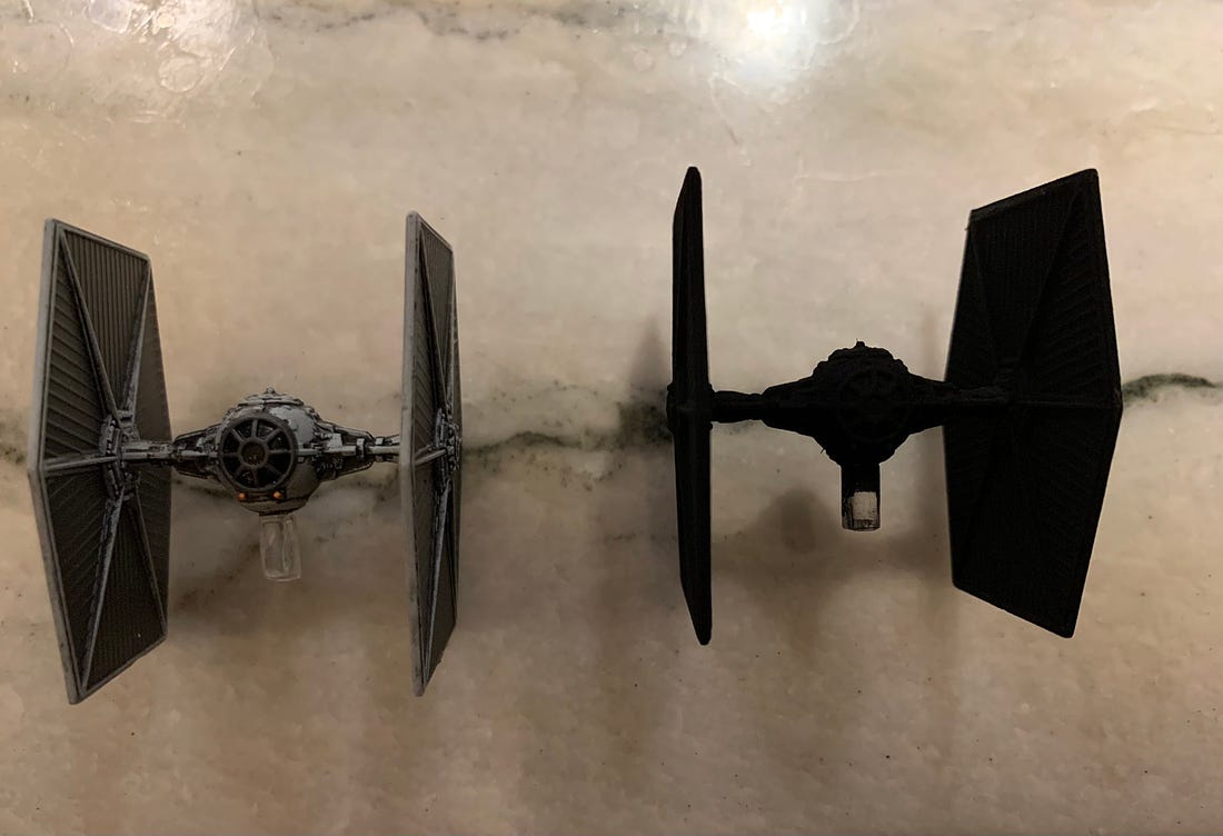 Image shows two models of TIE fighters. The one in left is painted in the traditional blue-grey scheme, while the one in the right has been entirely coated in a completely black paint.