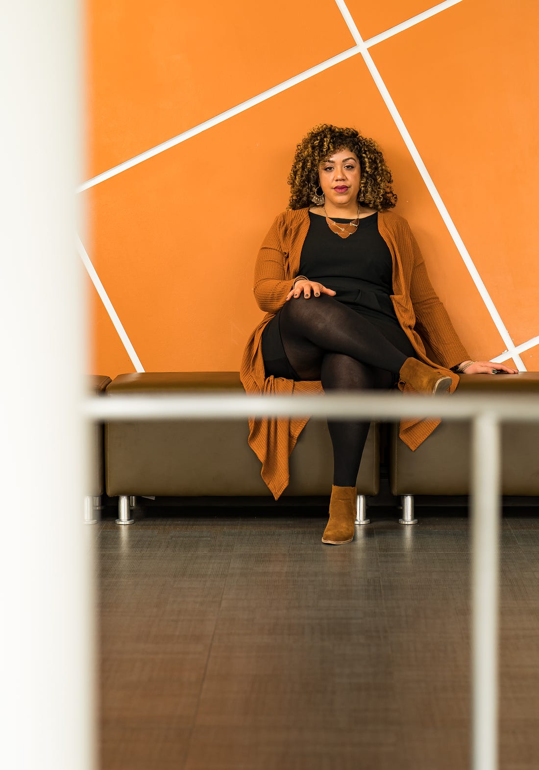 A photo of Dr. Jennifer Mullan sitting on a bench against a wall with with large orange square tiles at an angle.