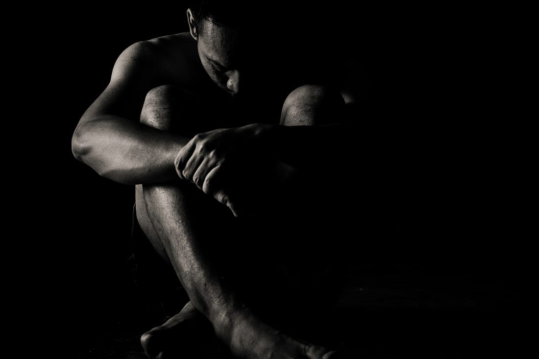 black and white photo of a depressed man crouched in the dark for article by Larry G. Maguire