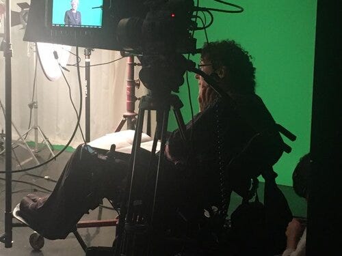 Writer Susan Nussbaum, sitting in a chair by a green screen, as a film is being made in front of her.