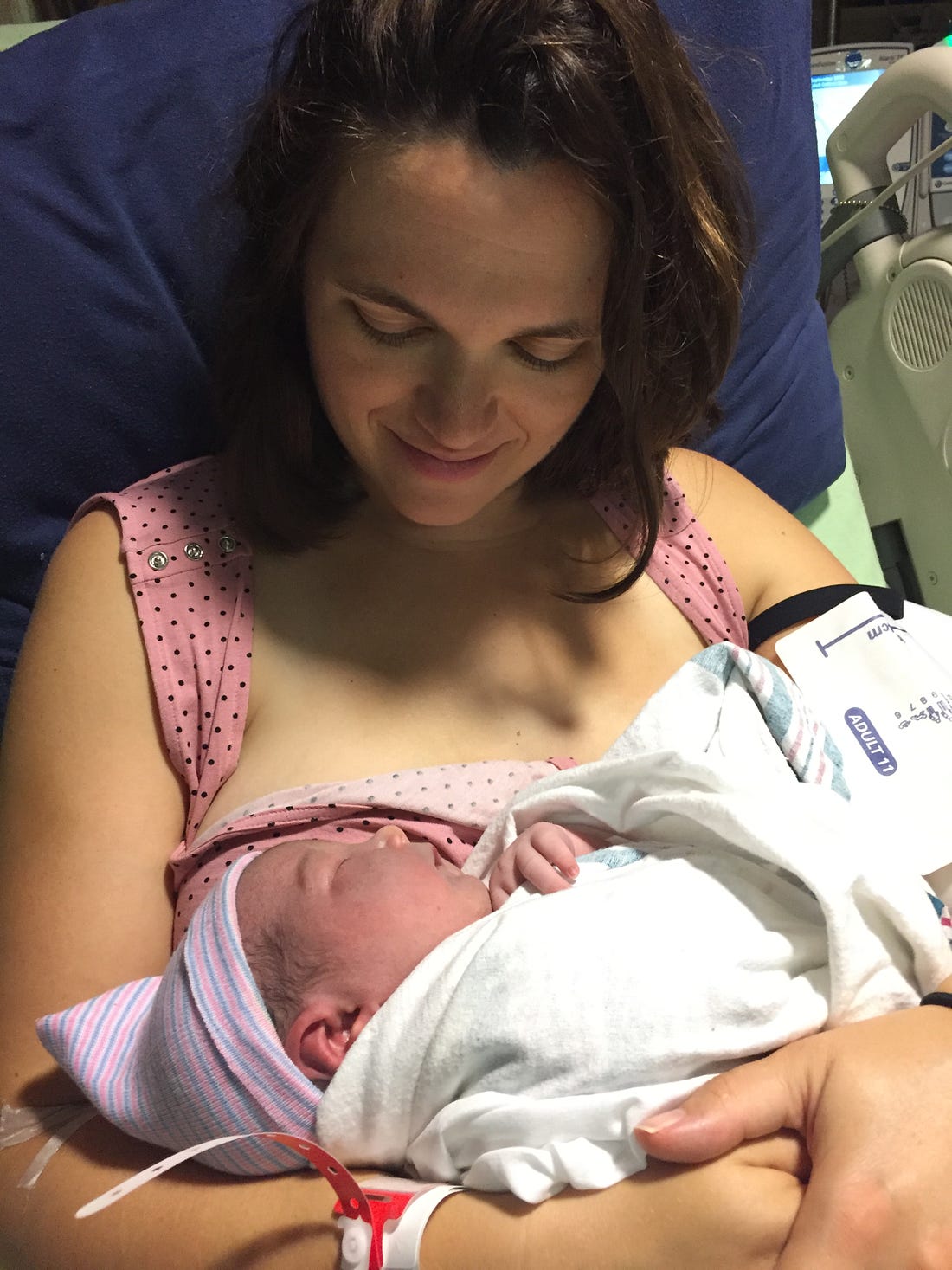 Photo shows a woman with brown hair in a hospital bed staring at a newborn.