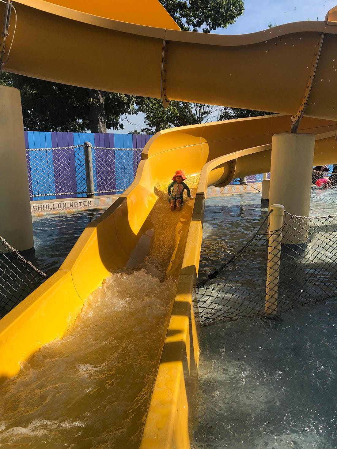 Photo shows a 4 year old in an orange hat on a winding yellow water slide.