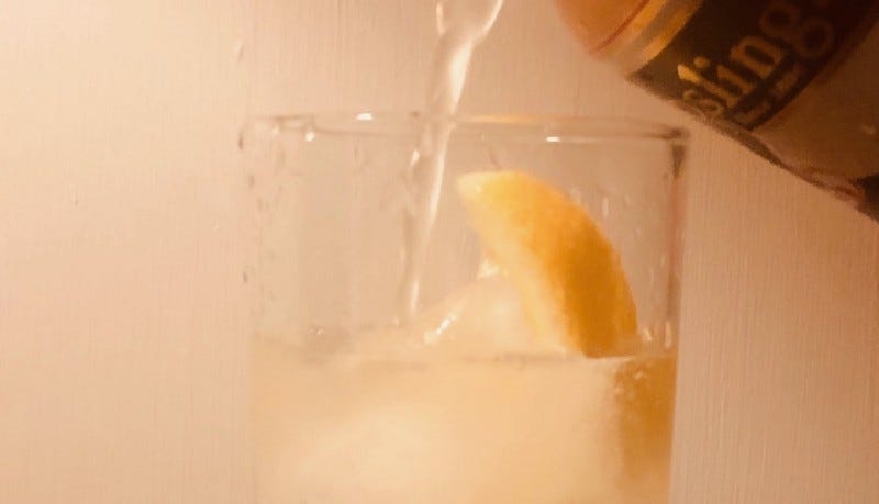 Closeup of a clear liquid being poured into a glass with a lemon wedge in it.