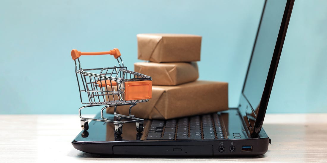 Mini shopping cart and packages on top of a laptop (an illustration).