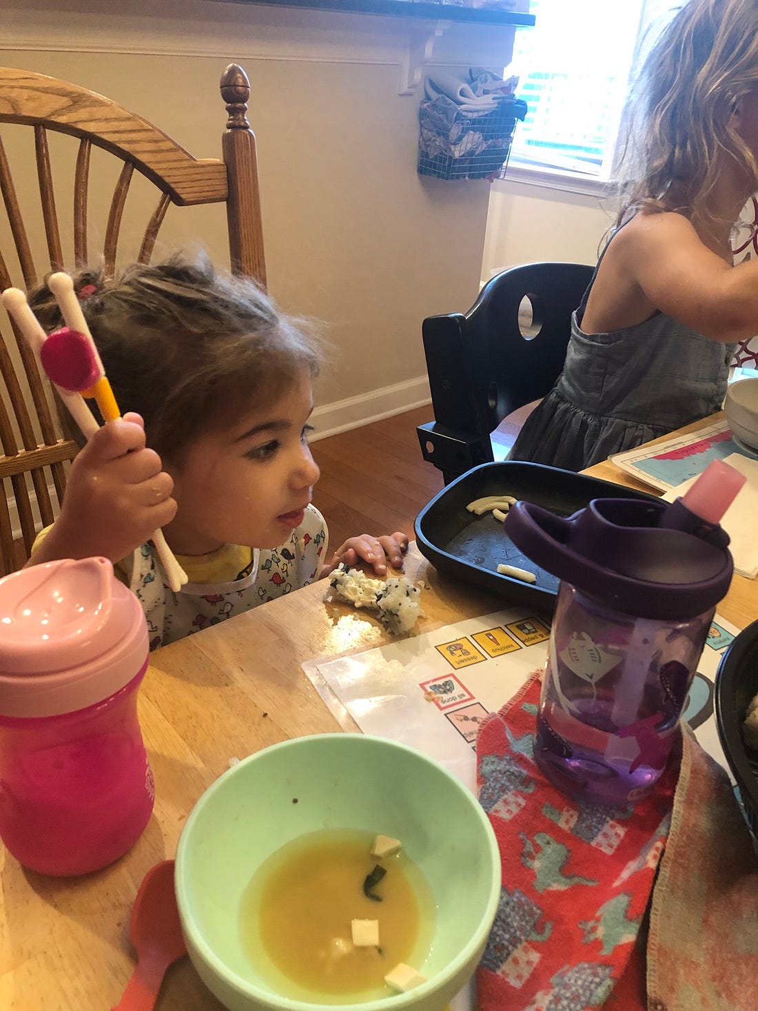 photo of a toddler holding a pair of chopsticks sitting at the dining table