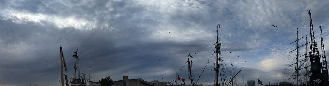 A pretty rubbish photo of Bristol harbour that is mostly the sky with some masts and some tiny dots that are balloons above