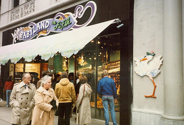 The Babyland on Fifth storefront. Adults linger outside. A cartoon stork delivering a baby is bolted to the building outside.