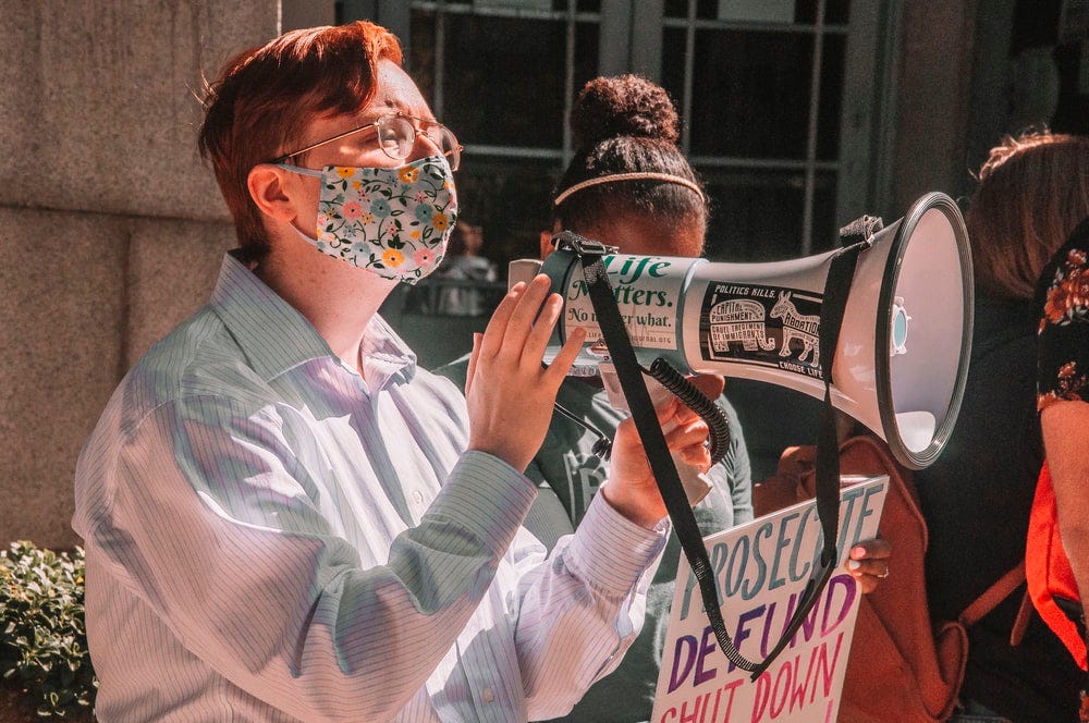 An activist protests in a mask, talking to a megaphone