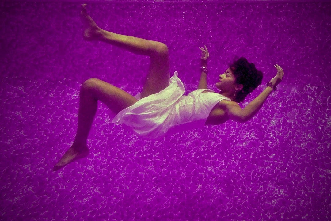 Underwater Fashion Shoot of model Savanna comfortably floating underwater in a purple pool.