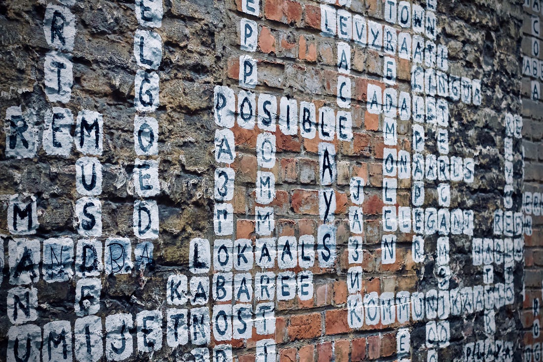Image of scrabble painted on a wall for article titled “words just don’t cut it” by Larry G. Maguire