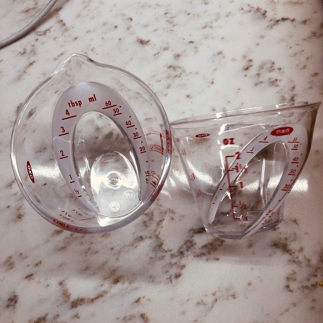 Two mini-measuring cups, with markings for several different units of measure