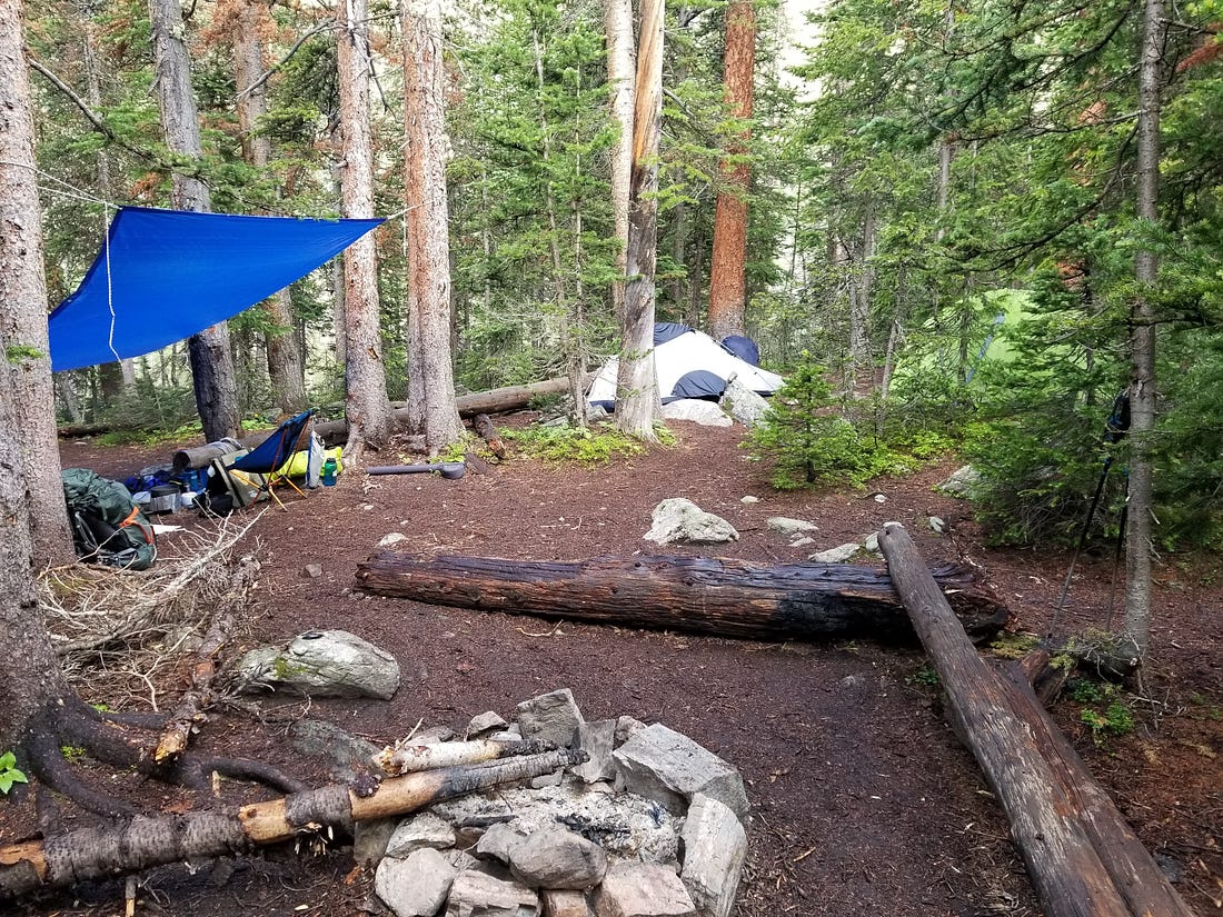 a small campsite built around a fire pit. Tents are recessed in the background, far away from the cooking area.