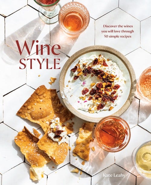 Cover for Kate Leahy's cookbook Wine Style; image is of a white tile background with multiple glasses of wine surrounding a ceramic bowl of white dip, topped with nuts, and several broken crackers.