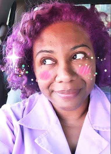 Selfie of Patricia. Her hair is bright purple and she is looking off to the side. She is wearing a lavender jumpsuit but the image is only from the chest upward. There is a filter applied that makes her have pink cheeks and glittery stars around her face.