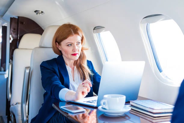 Businesswoman traveling by corporate jet Business travel. Elegant mature businesswoman sitting in private airplane and using a laptop. private jet stock pictures, royalty-free photos & images