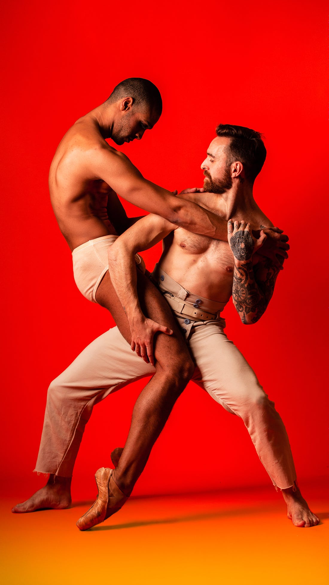 Two ripped male dancers embrace each other.