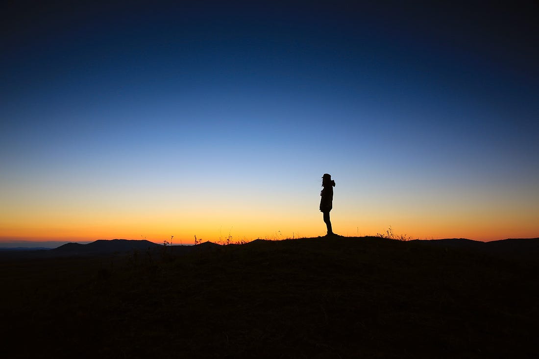 Image of a silhouette of a person standing on a hill at dusk for article titled “the illusion of free will”