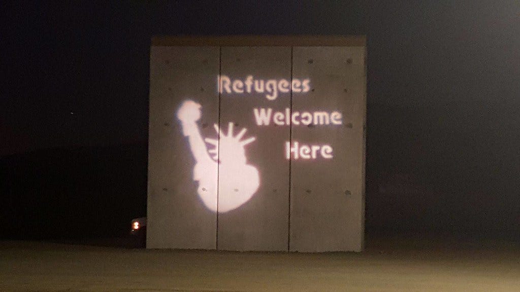 Refugees Welcome Here on Border wall with San Diego Solidarity Brigade Guerrilla Light Projection
