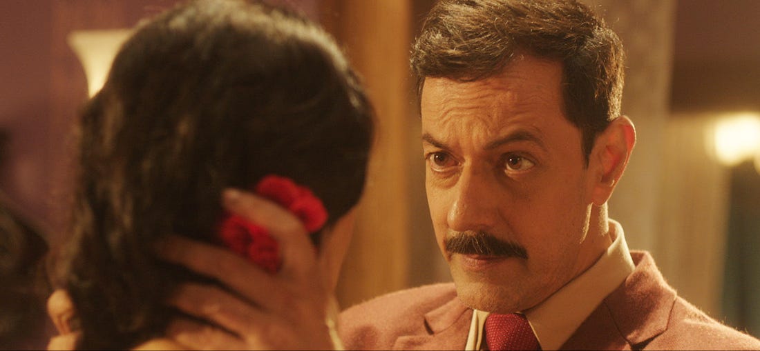 From the film "RK/RKAY": A man with a moustache speaks and looks into the eyes of a woman whose back is to the camera.