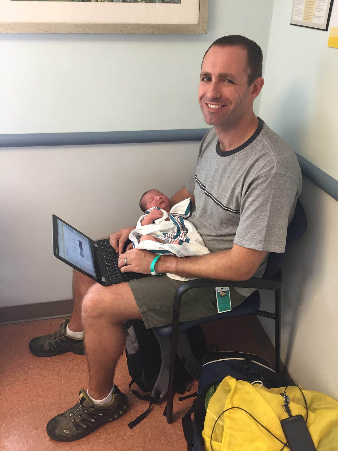 Photo of a man holding a baby while typing on a laptop.