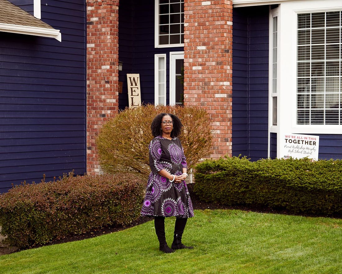A woman in a print dress stands on the lawn of a house.