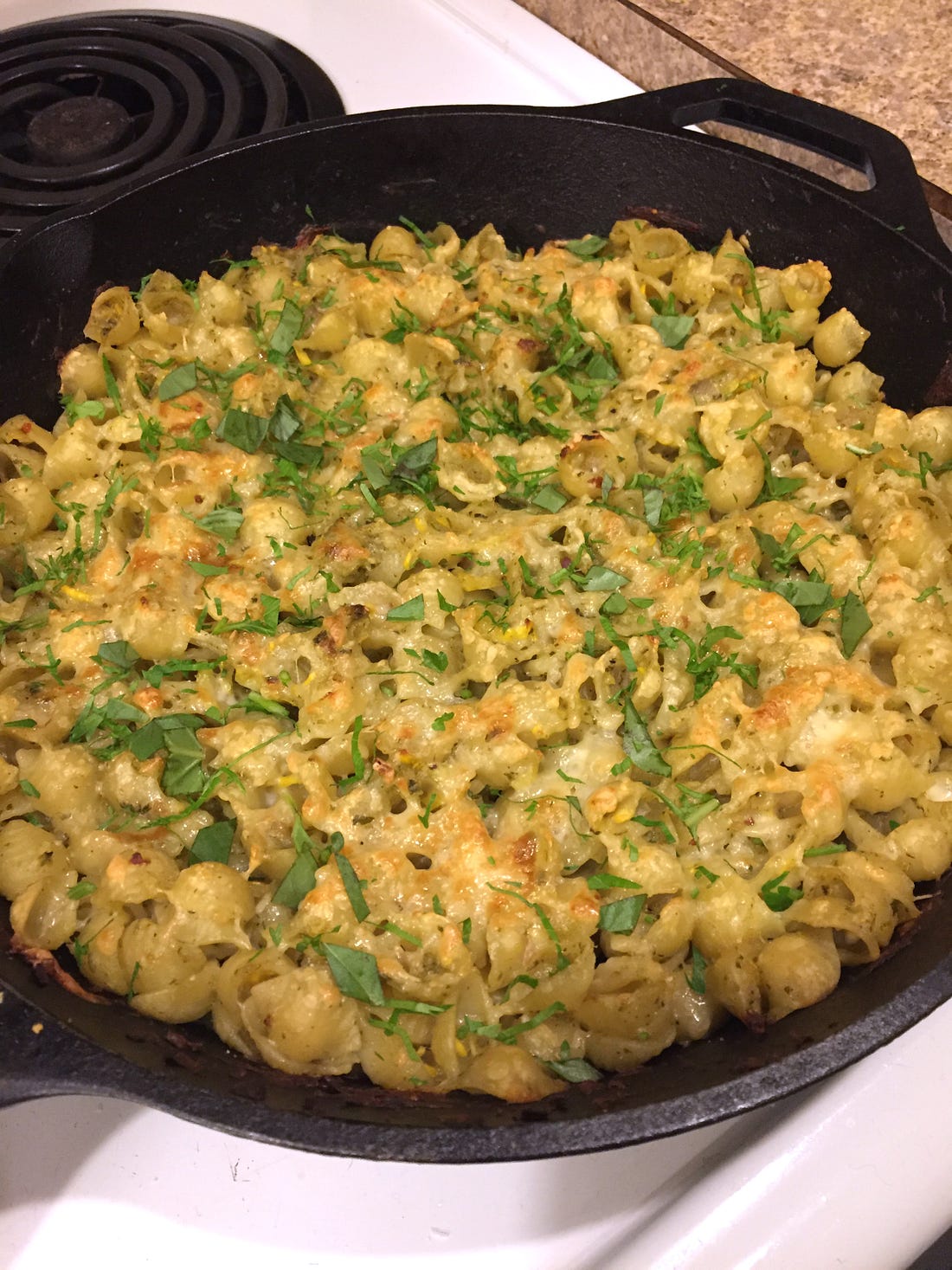 a cast-iron pan full of baked pasta shells. The cheese on top is browned, and sprinkled with parsley.