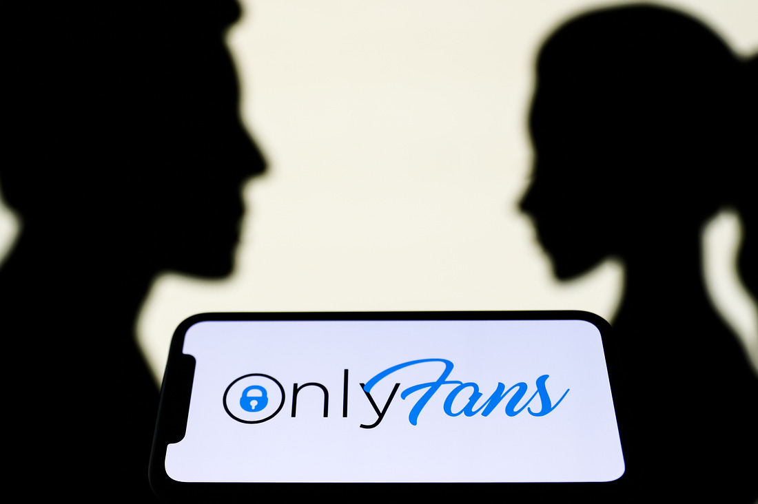 OnlyFans logo displayed on a phone screen is seen with paper silhouettes looking like a man and a woman in the background in this illustration photo taken in Krakow, Poland on August 25, 2021. (Photo by Jakub Porzycki/NurPhoto via Getty Images)