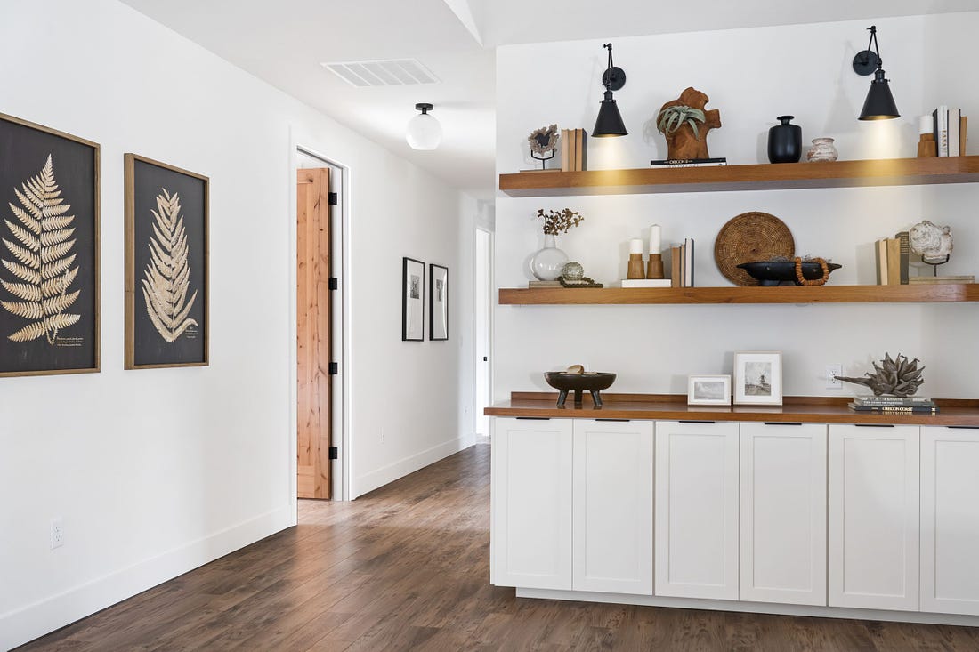 White walls, black fixtures and wood accents decorate a living space leading to an extra-wide hallway. 