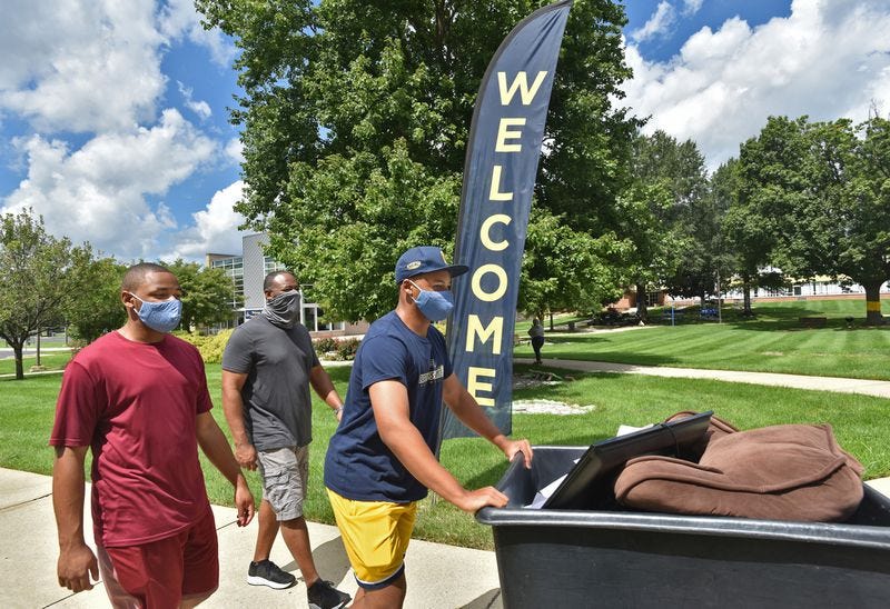 Toran Smith, 19, a returning second-year student at Coppin State University, pushes a cart with his belongings toward his dorm, accompanied by his brother Cameron, left, and father, Sam Smith behind them. They drove to campus from Plainfield, New Jersey. Aug. 23, 2020. (Amy Davis/Baltimore Sun)