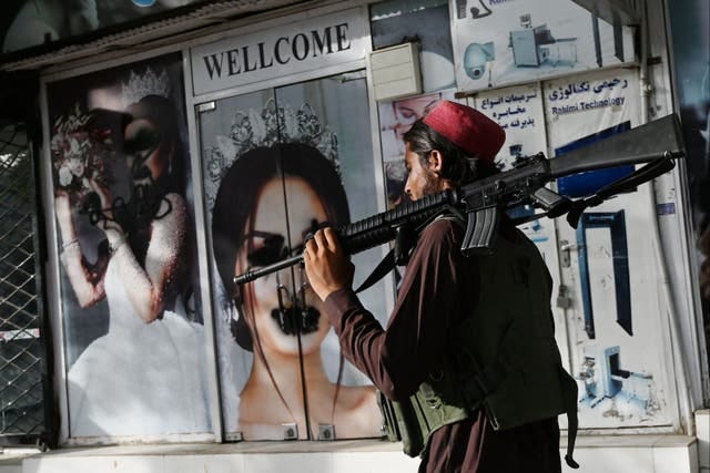 <p>Crackdown: a Taliban fighter walks past a beauty salon in Kabul where the posters of women on the shop front have been defaced</p>