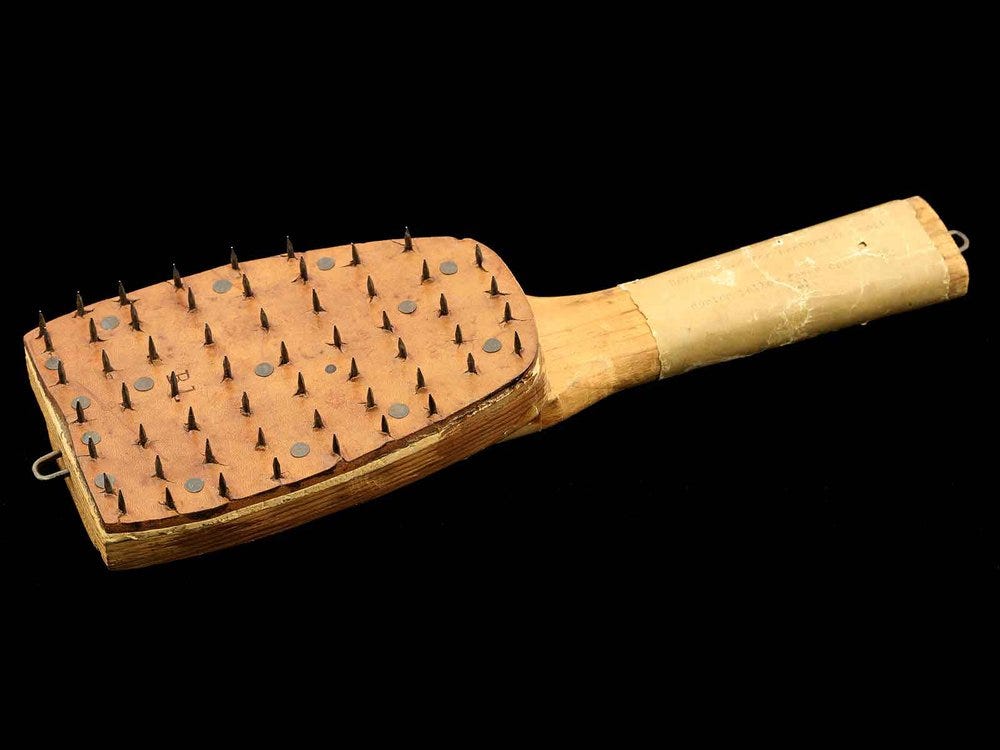 wooden paddle covered in rows of spikes