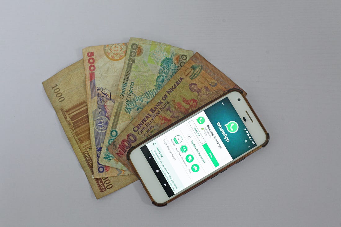Photo of a phone with WhatsApp open laid on top of currency fanned out underneath it. Benjamin Dada / Unsplash