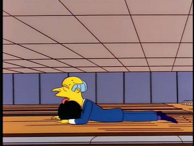 A screenshot from The Simpsons, showing Mr. Burns lying on the bowling alley floor, his tongue lolling out over a bowling ball, after he fails to throw it more than a foot.