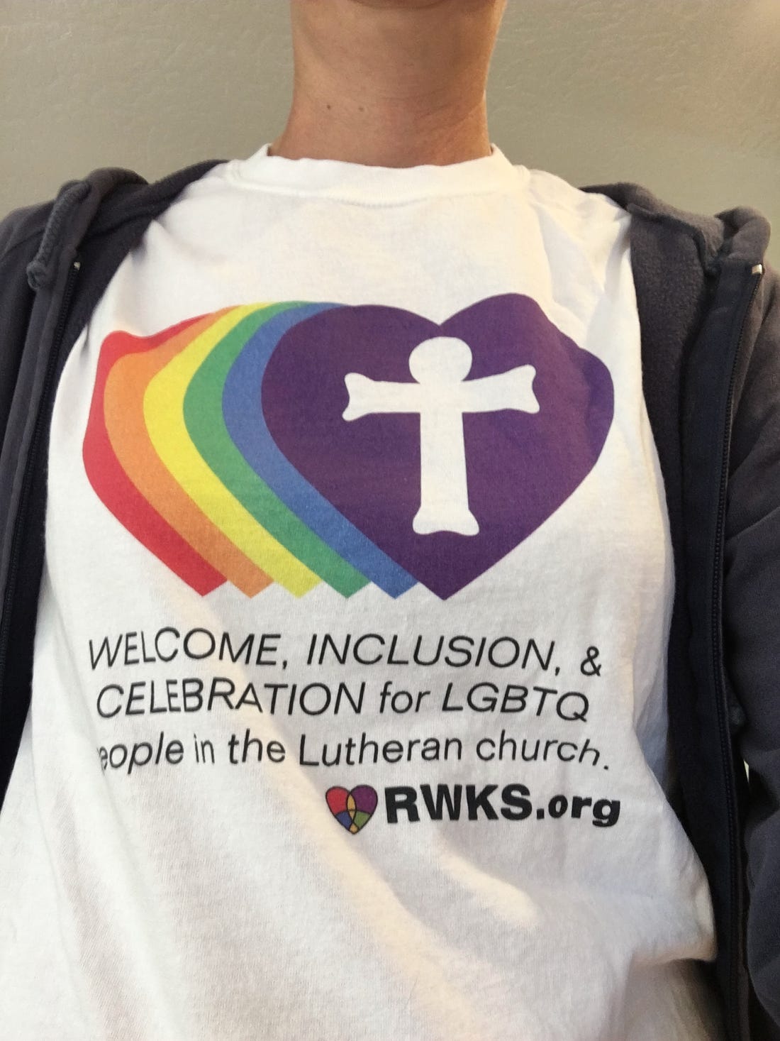 Photo of a t-shirt front with rainbow hearts in a row and the last one has a cross inside it.