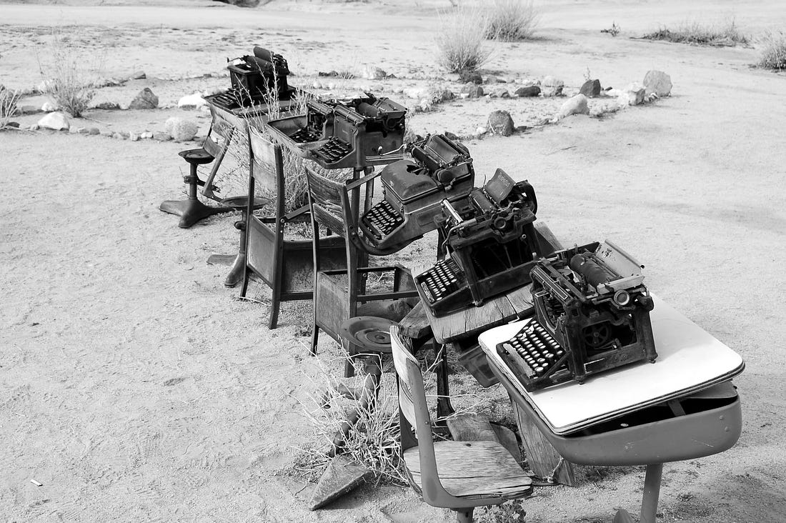 Image of old typewriters atop old desks outside in the sand