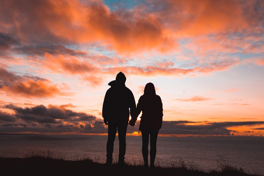 Man and woman holding hands looking at sunset