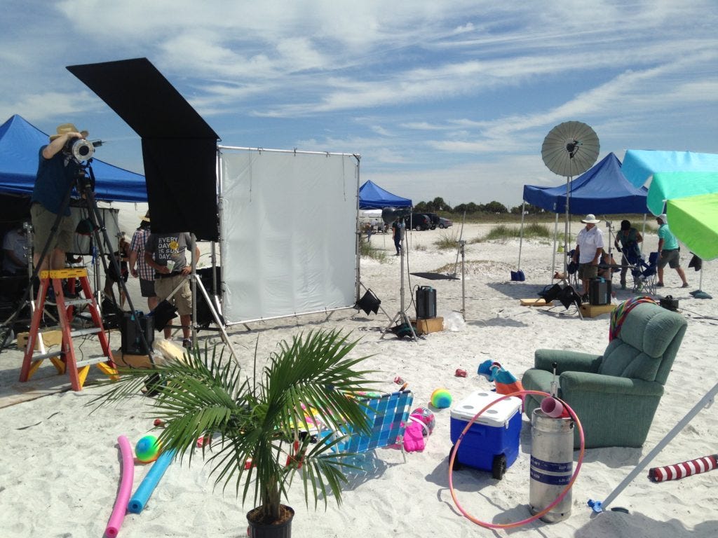 Behind the scenes photo on a beach with pop up tents, strobe lighting, and a lot of light stands. Set safety during this shoot meant not getting sand in the gear.