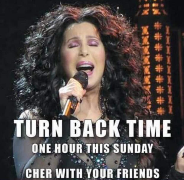 Photo of the performer Cher singing into a microphone. There is white text at the bottom of the image that says, "Turn back time one hour this Sunday. Cher with your friends"