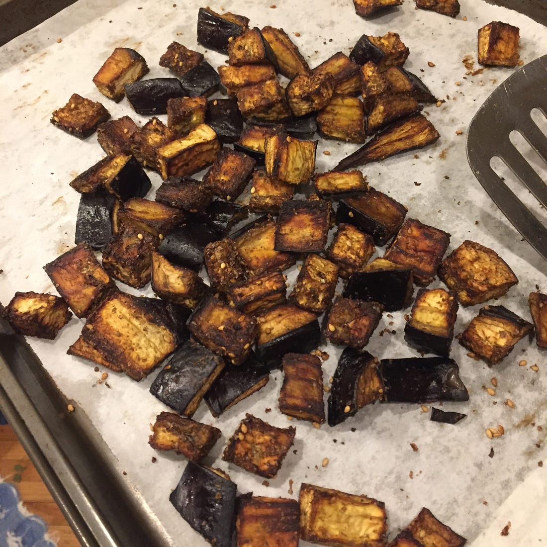 a parchment-lined pan full of cubes of browned roasted eggplant. Sesame seeds from the za'atar are visible throughout.