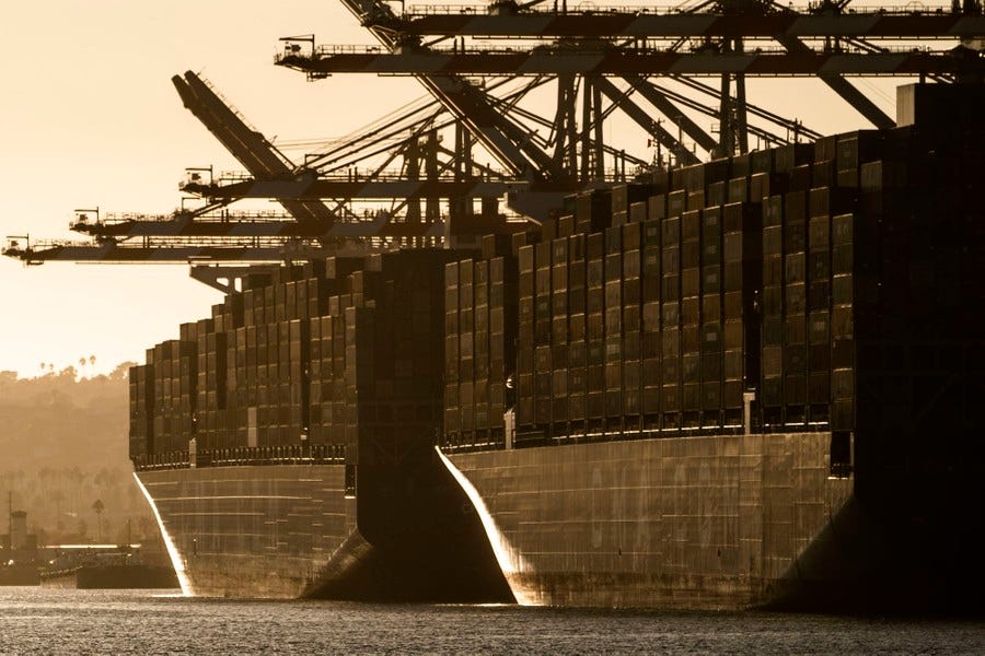 Two large (and full) container ships are seen moored at a port at sunset.