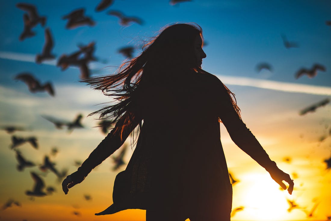 silhouette of a woman against a setting sun with birds in the background for article titled “Maslow Peak Experience”