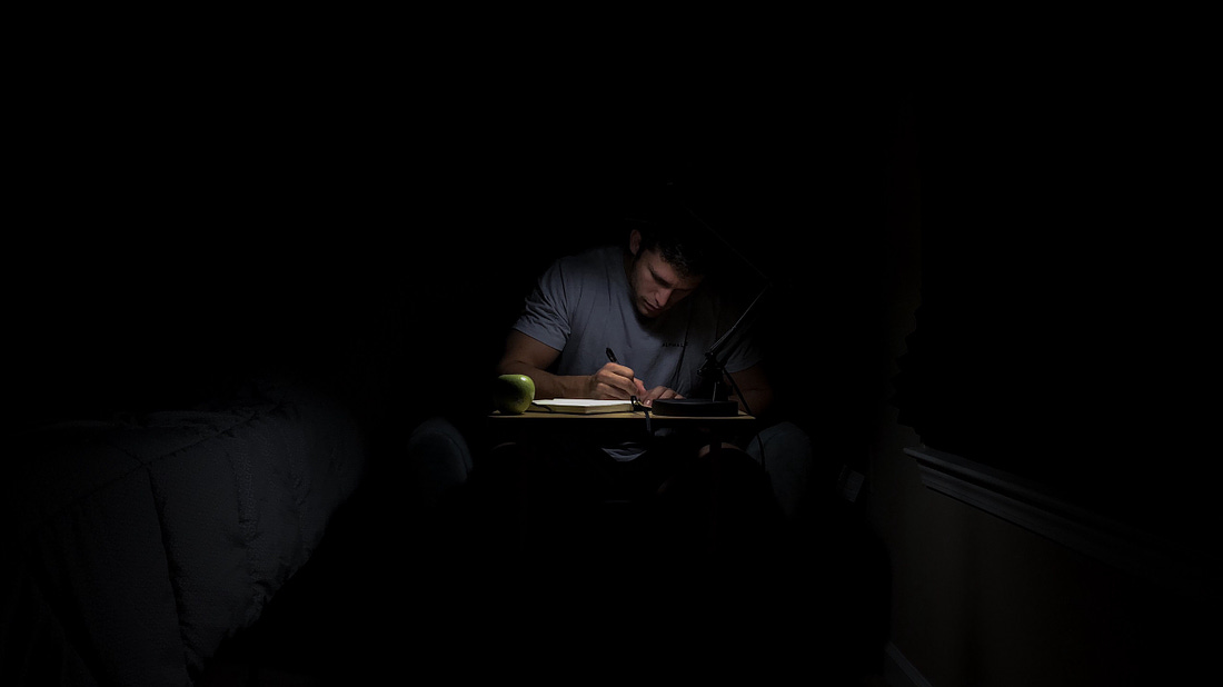 Man sitting in the dark, writing, for article titled “The Book That Never Gets Written” on The Reflectionist