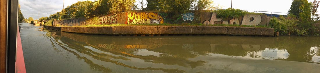 A view of the water from a canalboat looking at a wall covered in graffiti