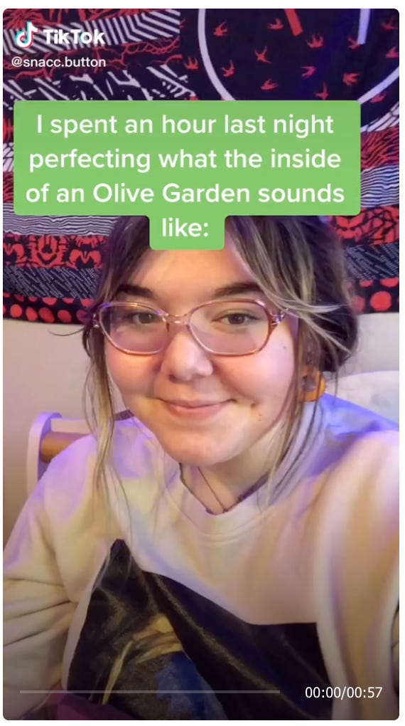 TikTok video screenshot of a girl smiling slightly, below the caption “I spent an hour last night perfecting what the inside of an Olive Garden sounds like:” Please click for the TikTok, it’s an audio masterpiece.