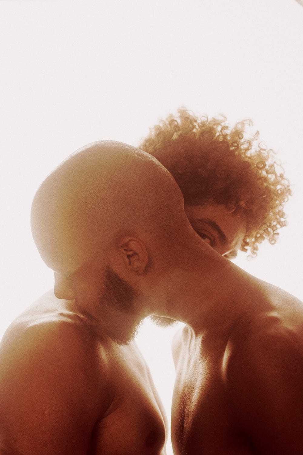 two naked men embracing and kissing while one looks at the camera