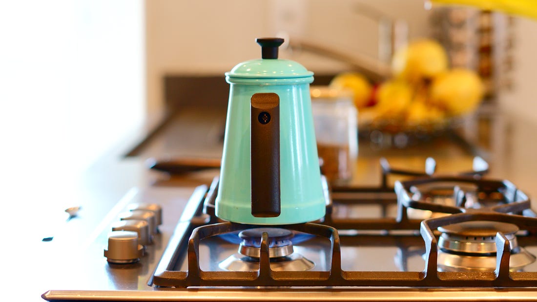 A teal kettle sitting on a lit gas stove