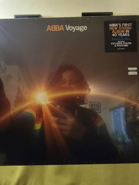 Photo of the album cover of ABBA Voyage. It is still it it's plastic and you can see Patricia's reflection. She is wearing a rainbow cardigan.